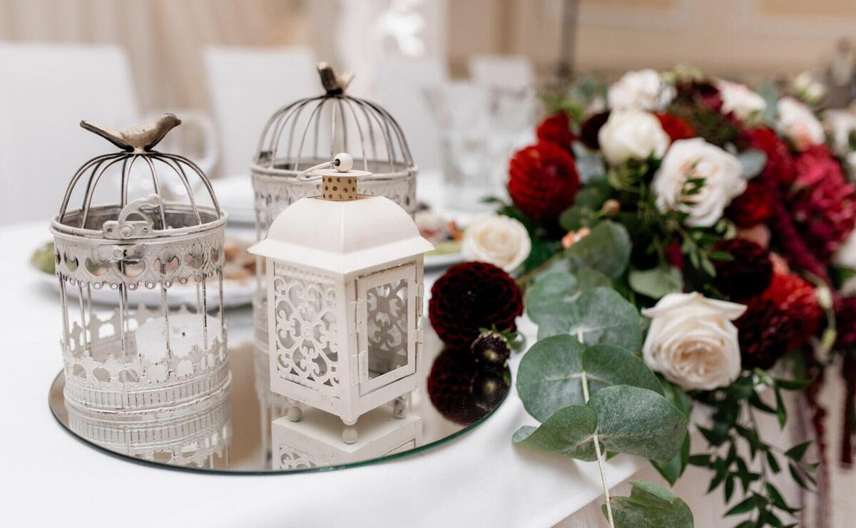 Floral composition with eucalyptus, white and bordeaux roses on the table and metal cages on a mirror tray
