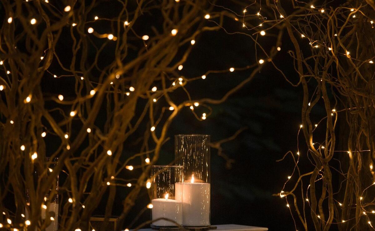 Tall vases with white candles stand under shiny branches