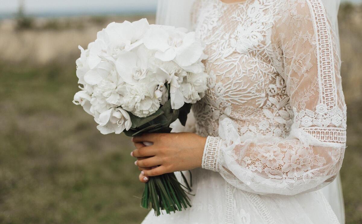 Wedding bouquet made of white peonies in the bride's hand outdoors