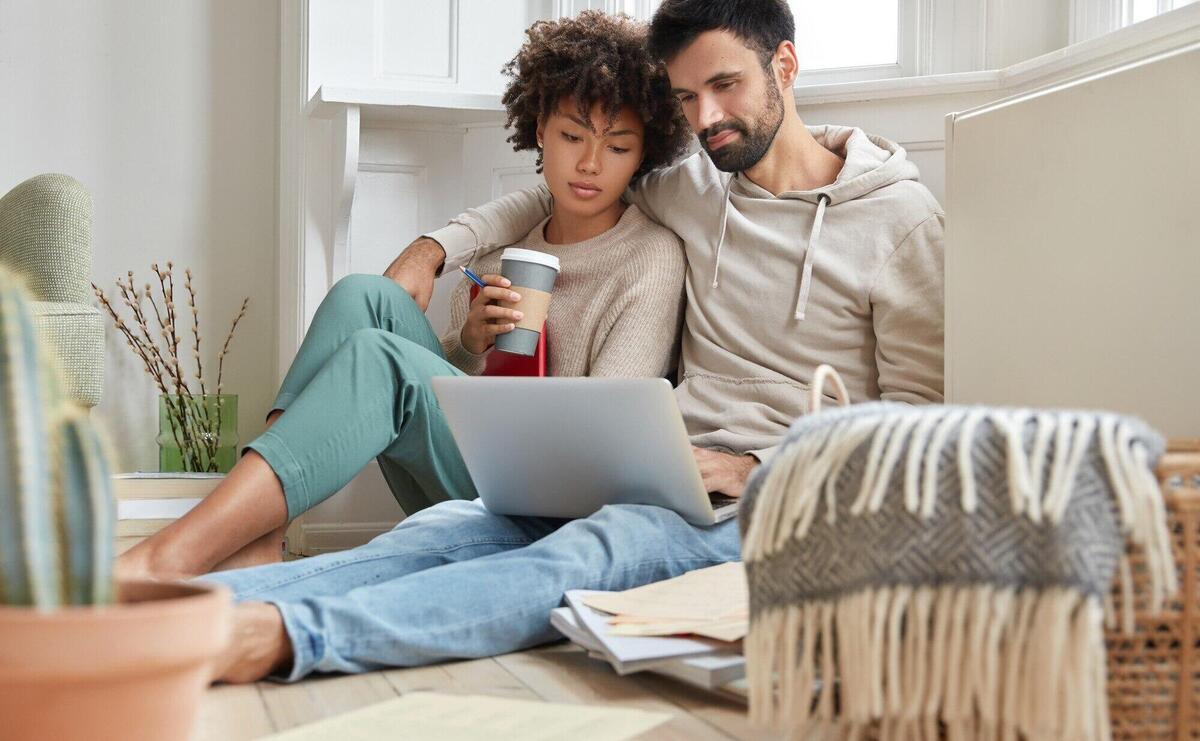 Lovely mixed race couple embrace each other, sits on floor, feel relaxed while watch movie on laptop computer