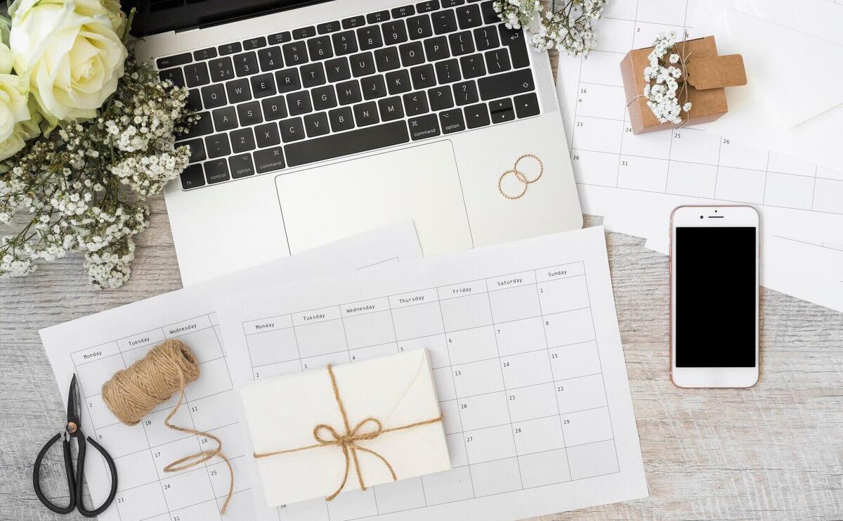 Envelope; calendar; laptop; flowers; smart phone; spool; scissor and spiral notebook on wooden desk