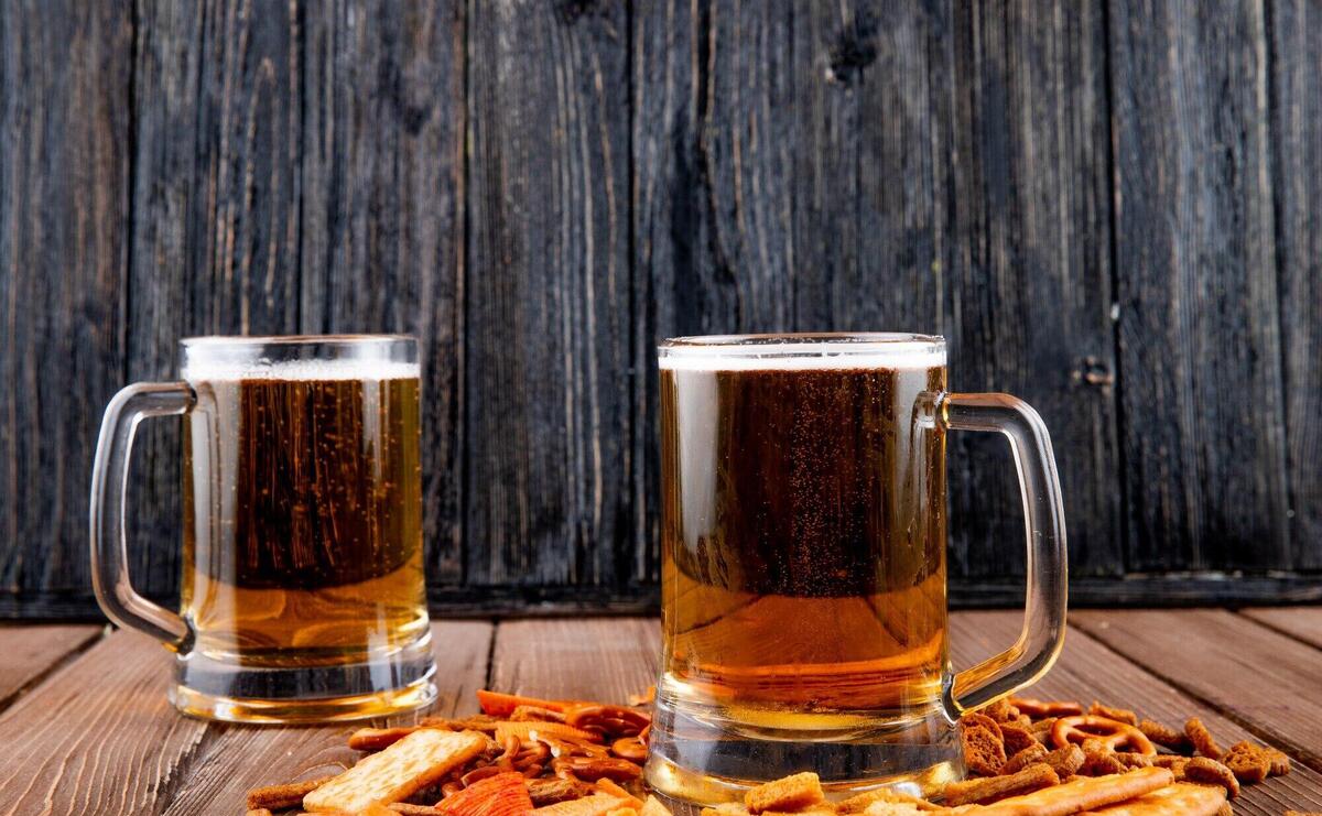 side view Mugs of beer with hard chuck chips and crackers on wooden table