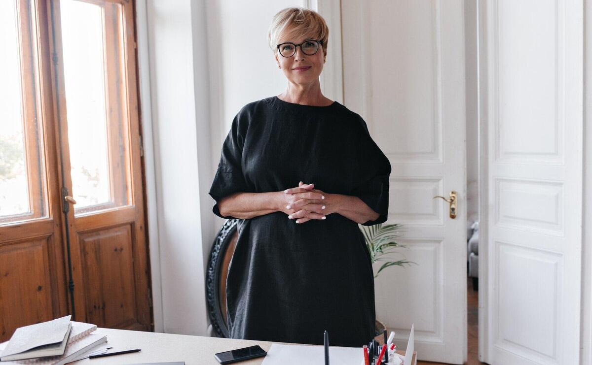 Lady in black dress and eyeglasses looks into camera in office