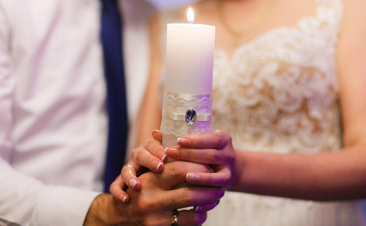 Bride and groom holding candle. Close-up shot of hands