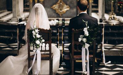 Bride and groom sitting on chairs on their wedding day, from the back