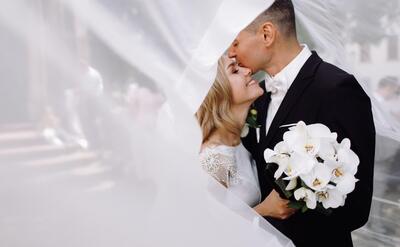 Groom in black tuxedo hugs tender stunning bride while they stand