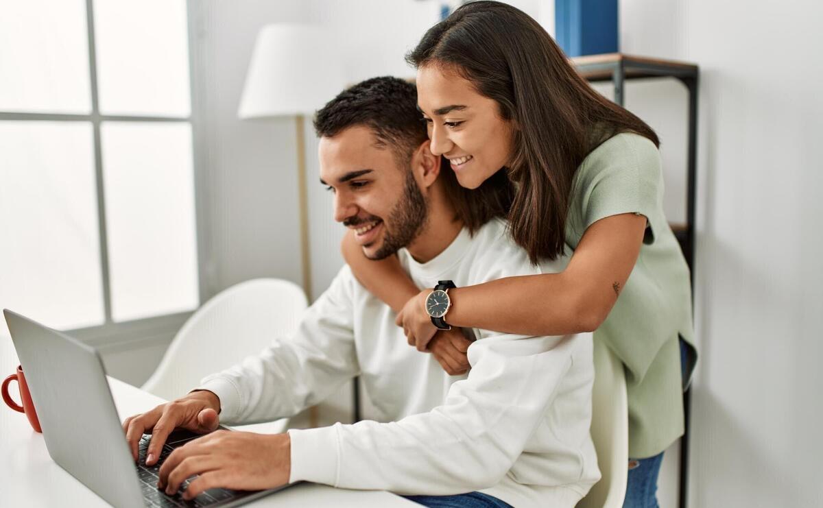 Young latin couple using laptop and drinking coffee at home.