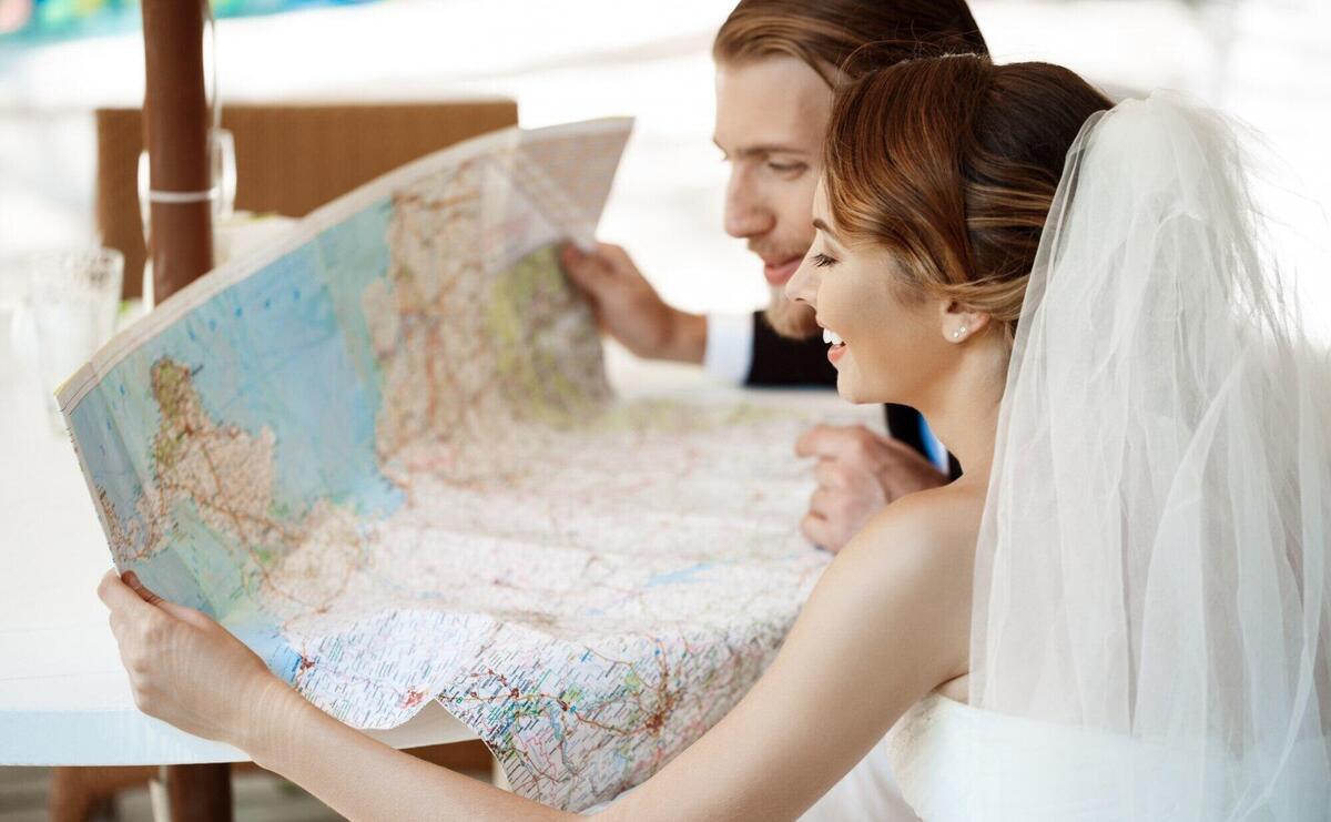 Young beautiful newlyweds smiling, choosing honeymoon trip, looking at map.