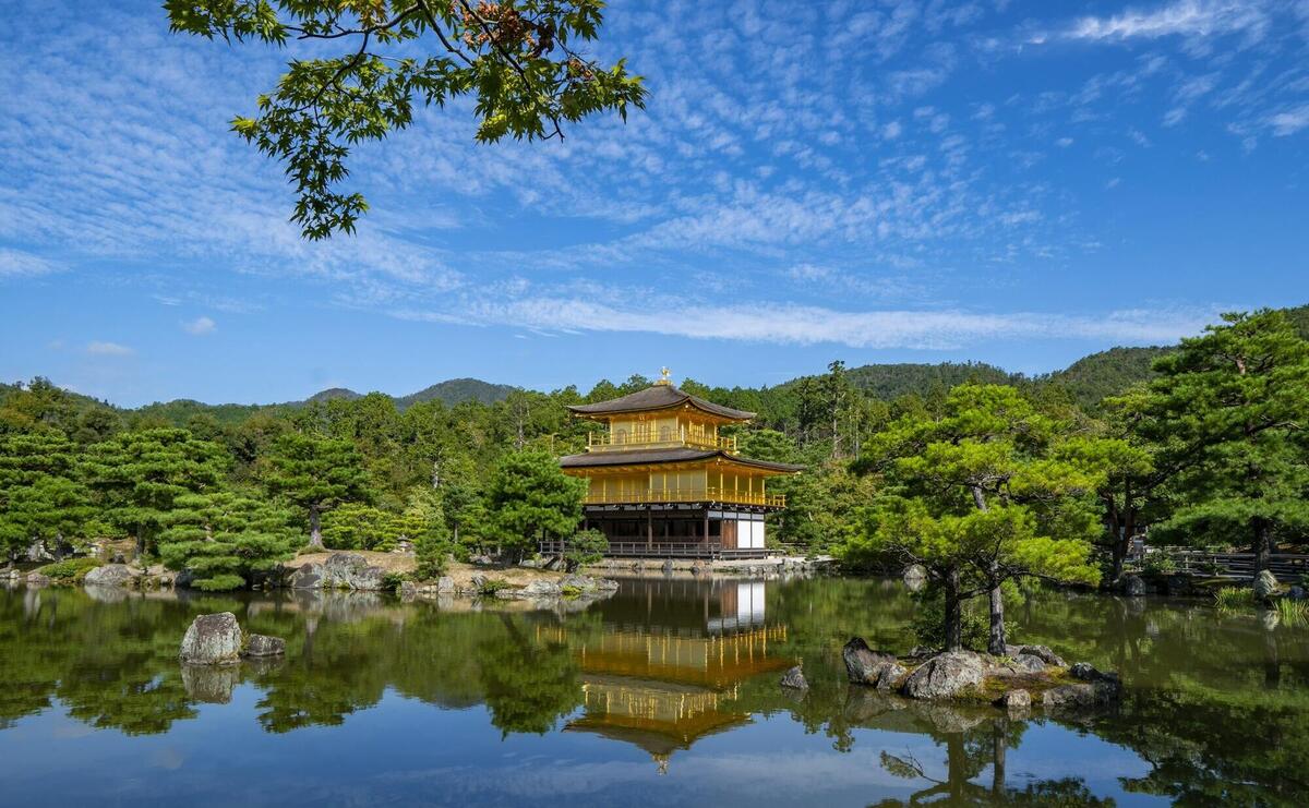 Kinkaku-Ji in japan surrounded with tall and green trees near body of water under blue and white sky during daytime