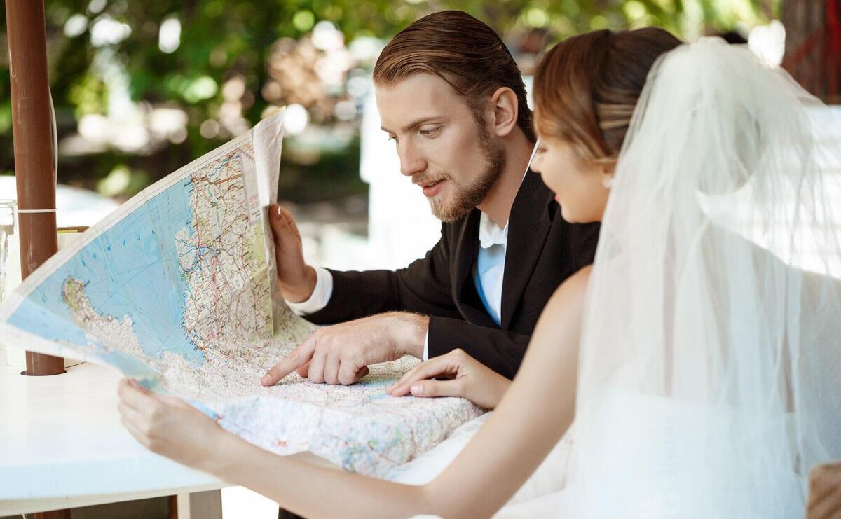 Young beautiful newlyweds smiling, choosing honeymoon trip, looking at map.
