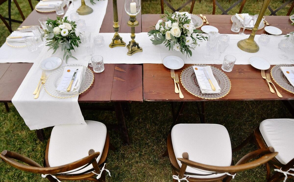 Top view of brown chiavari chairs, glassware and cutlery on the wooden table outdoors, with white eustomas bouquets