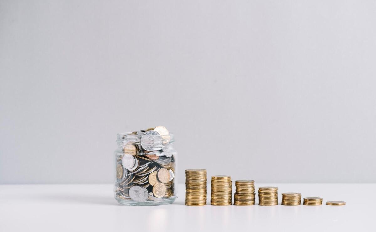 Glass jar full of money in front of decreasing stacked coins against white background