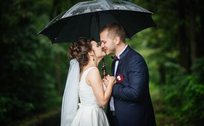 Bride and groom holding umbrella in hands looking at each other kissing and smiling
